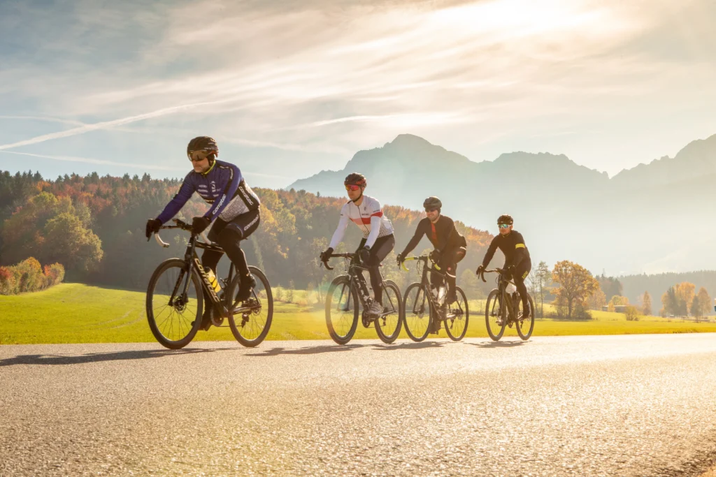 Vier Rennradfahrer auf herbstlicher Landstraße vor Bergpanorama