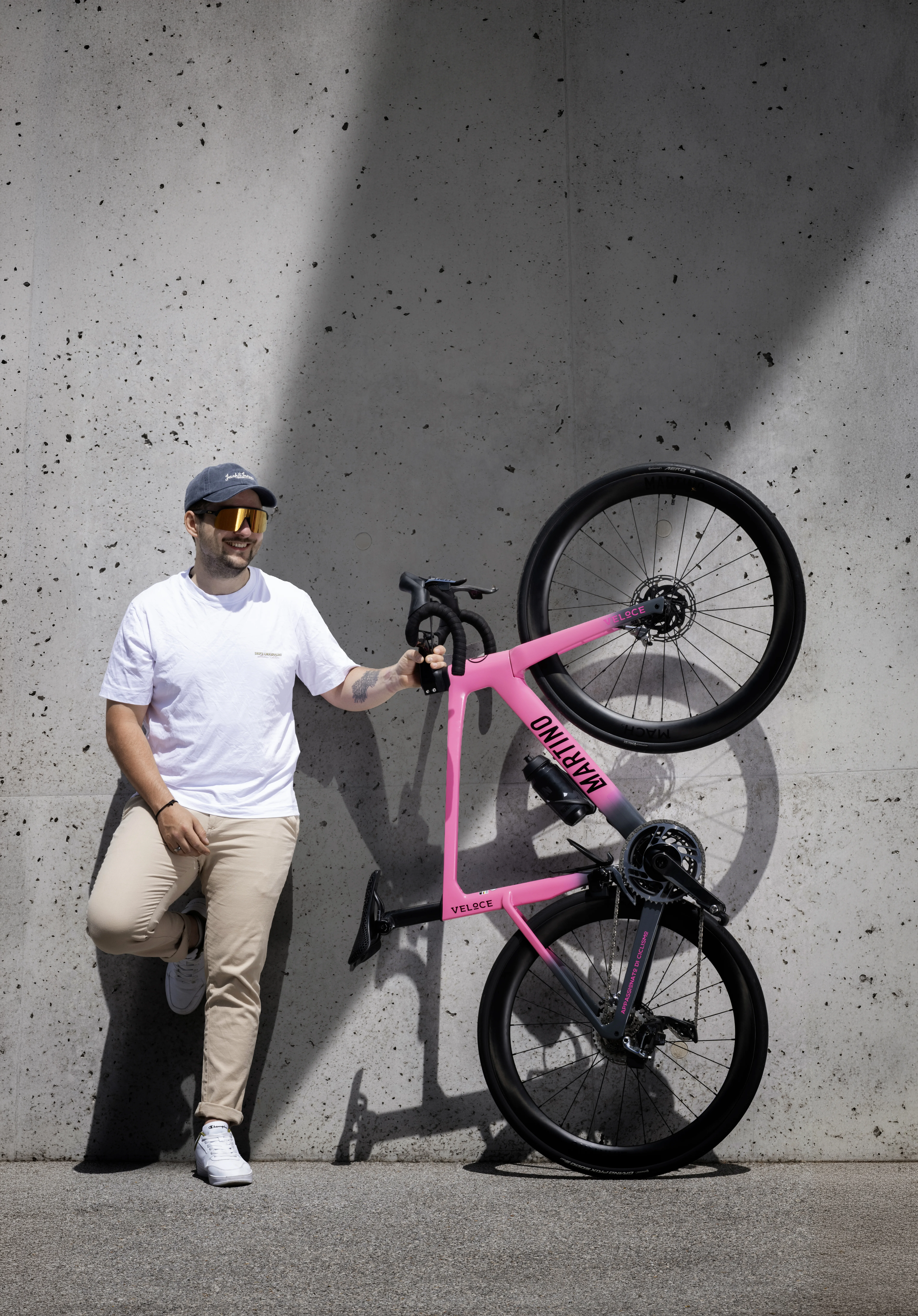 Luca Martino mit einem Martino Veloce Custom-Rennrad in Pink vor einer Betonwand